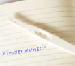 Ein Schwangerschaftstest und ein Notizbuch mit dem Wort Kinderwunsch